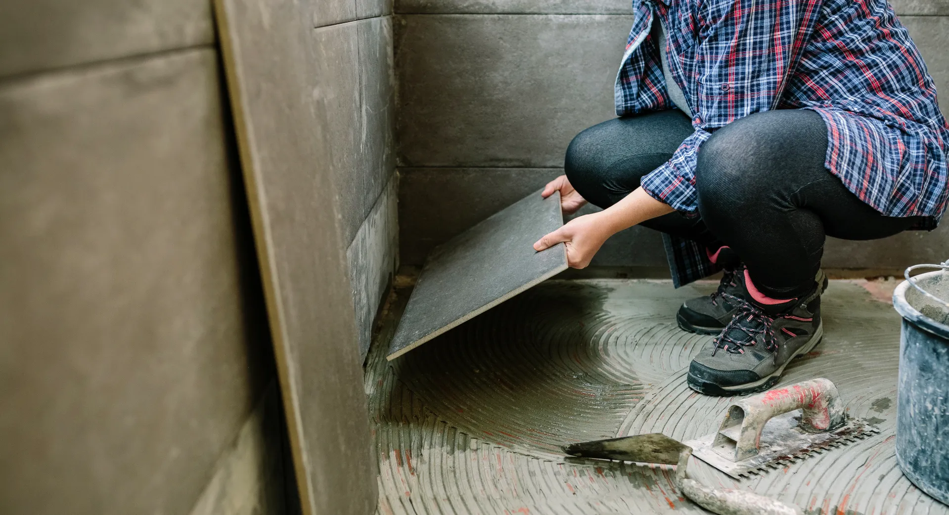 Female builder laying new tile floor during basement waterproofing renovation in Toronto